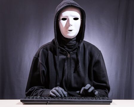 A hacker sits in front of the keyboard of a computerの写真素材