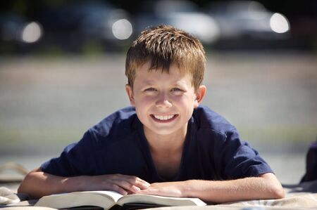 young boy on a beach reading a bookの写真素材