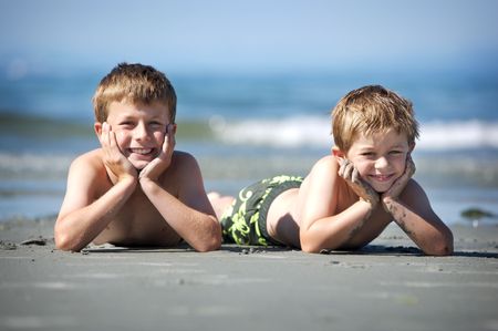 two young boys laying on a sandy beachの写真素材