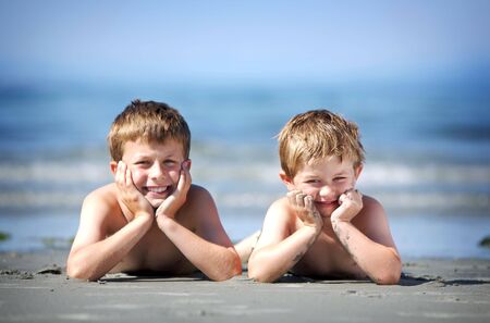 two young boys laying on a sandy beachの写真素材