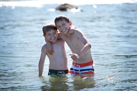 two young boys standing in the ocean arm in armの写真素材