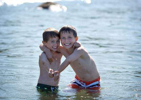 two young boys standing in the ocean with thumbs upの写真素材