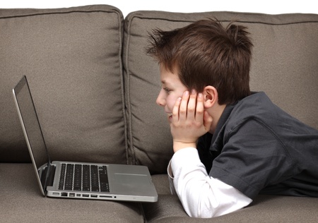 cute young boy with a laptop on a couchの写真素材