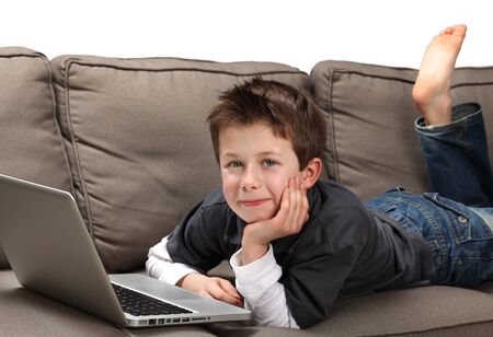 cute young boy with a laptop on a couchの写真素材