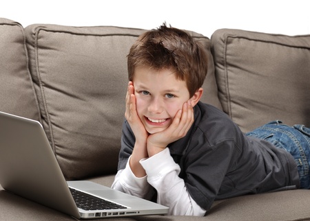 cute young boy with laptop on a couchの写真素材