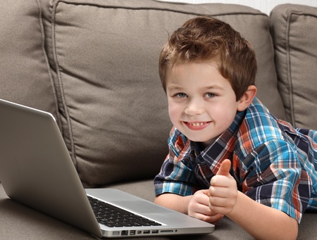 cute young boy with laptop on a couchの写真素材