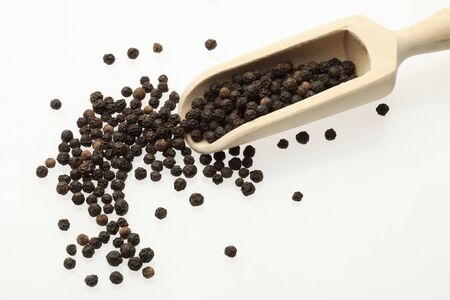 black peppercorns on a wooden spoon over whiteの写真素材