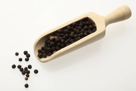 black peppercorns on a wooden spoon over whiteの写真素材