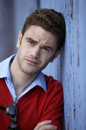 portrait of a young man leaning on a blue wooden wallの写真素材
