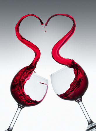 Red wine splashing out of two glasses in heart shapeの写真素材
