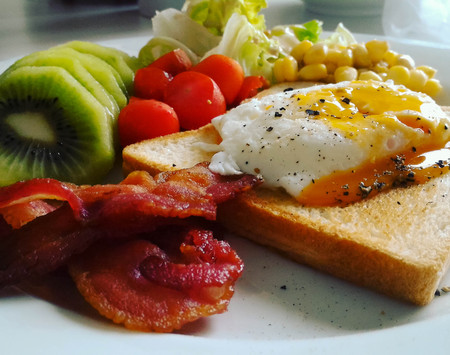 A breakfast dish, poach egg put on a toast with crispy bacon, kiwi , tomatoes and little bit corn.の写真素材