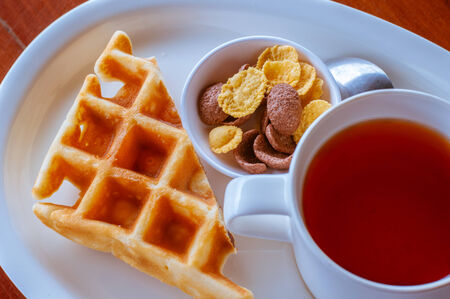 Cereal and waffle placed next to a tea cup