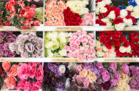 Colourful artificial flower made from plastic and fabric on shelf with flower name in thai alphabet.