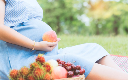 Pregnant woman holding apple fruit in the garden. Can use for healthy food concept background. (Vintage tone)の写真素材