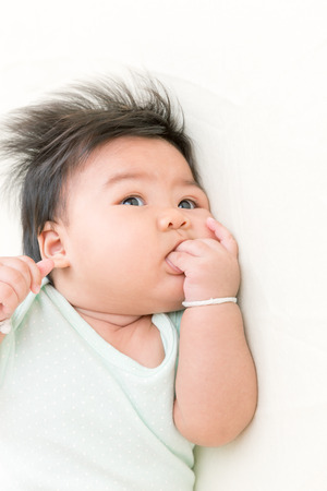 Adorable asian baby sucking thump on the bed. This is growth deveopment behavior.の写真素材