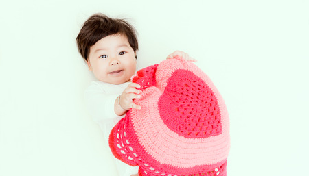 Adorable asian baby girl play red heart pillow on the bed for valentine background. (Vintage tone)の写真素材