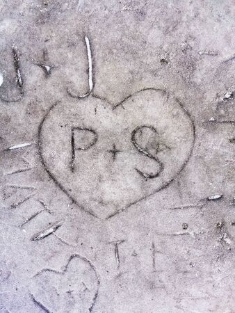 Carved love design in stone, heart with plus and letters on rock, carving, close up, gray background.の写真素材
