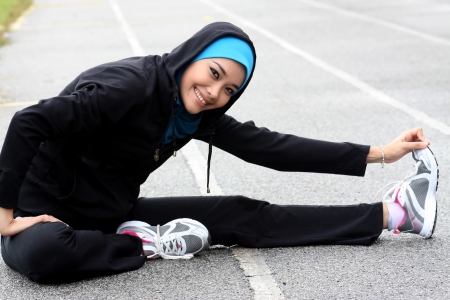 A pretty muslim woman athlete stretching her body at stadium trackの写真素材