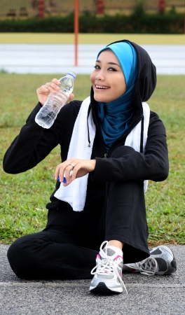 A pretty muslim woman athlete resting while drink a mineral waterの写真素材