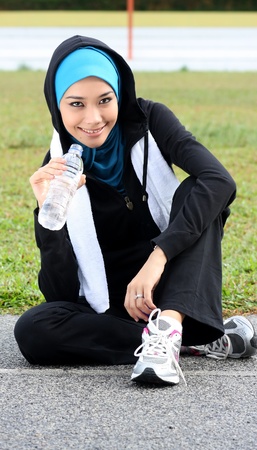 A pretty muslim woman athlete resting while drink a mineral waterの写真素材