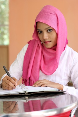 A beautiful muslim girls writing a diary book on the tableの写真素材