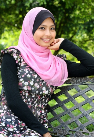 Young muslim woman is sitting on the bench in autumn park and looking at camera の写真素材