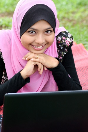 Portrait of young pretty muslim woman resting on mat at summer park using laptop の写真素材