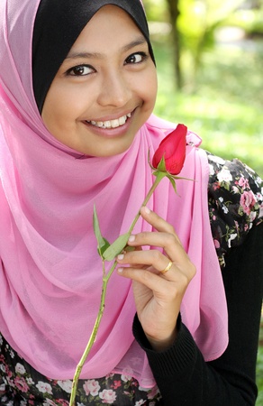 Portrait of beautiful young muslim girl holding a red rose flower at parkの写真素材