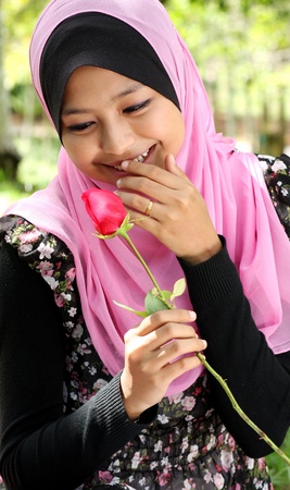 Portrait of beautiful young muslim girl holding a red rose flower at parkの写真素材