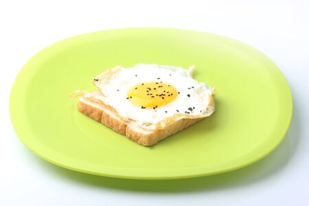 Fried egg on a slice of wholemeal bread with green plateの写真素材