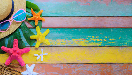 Starfish, sunglasses, hat and palm leaf on colorful wooden backgroundの素材
