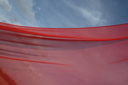 Red fabric waving in the wind against a blue sky with white clouds