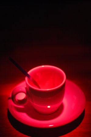 Cup of coffee on wooden table with red light in the dark