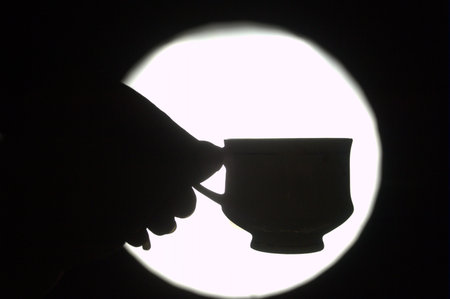 Silhouette of a hand holding a cup of coffee in the darkの写真素材