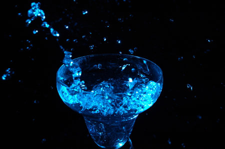 Blue water splash in a martini glass on a black background.