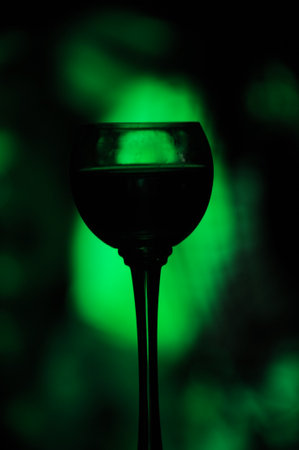 Glass of wine on a dark background with a green light in the backgroundの写真素材