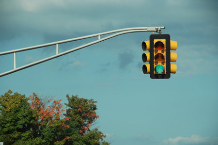 Traffic light on blue sky background with white clouds and trees.の写真素材