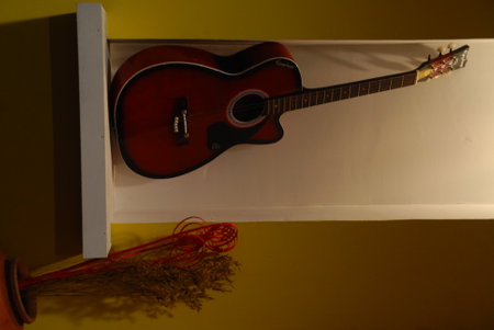 Acoustic guitar on a shelf in a room with a yellow wallの写真素材