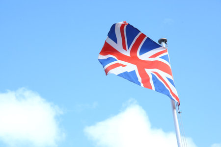 British flag waving in the wind against a blue sky with white cloudsの写真素材