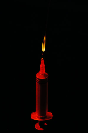 A red lit candle on a black background with a small flame.の写真素材
