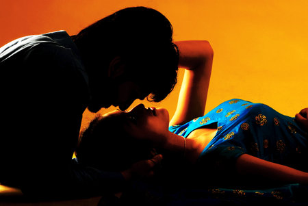 Silhouette of a young couple kissing and hugging on orange backgroundの写真素材