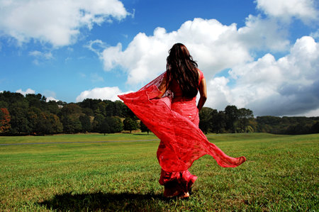 Young woman in a red dress dancing in the field on a sunny dayの写真素材
