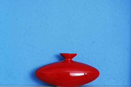Red ceramic vase on a blue wall background with copy space.