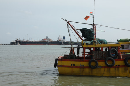 Fishing boat in the sea with cargo ships in the background.