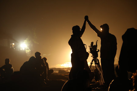 Silhouette of a cameraman with a camera on a tripod at sunset.の写真素材
