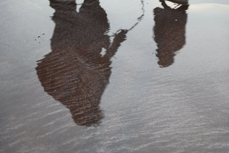 Reflection of a man in the water on a wet sand beachの写真素材