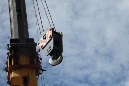 Crane hook against blue sky with white clouds. Construction equipment.の写真素材
