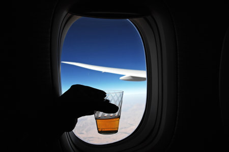 A glass of whiskey in hand on the background of the airplane windowの写真素材