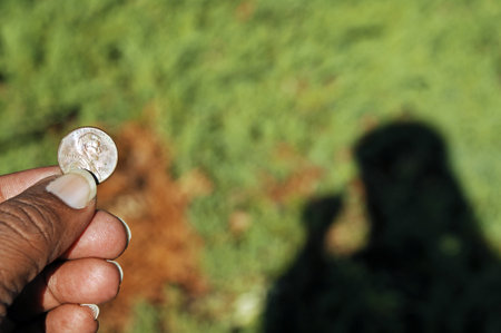 A coin in a hand with a shadow on the grass background.の写真素材