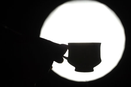 Silhouette of a man's hand with a cup of coffeeの写真素材